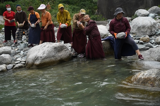 Tibetan Buddhist nuns lifting rocks at the stream